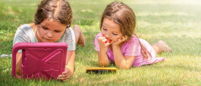 Children playing tablet and phone in the backyard in summer