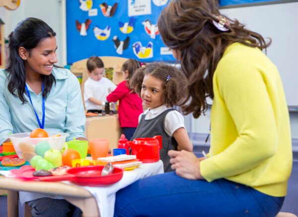 Teachers playing with plastic kitchen toys with their nursery students in the classroom.