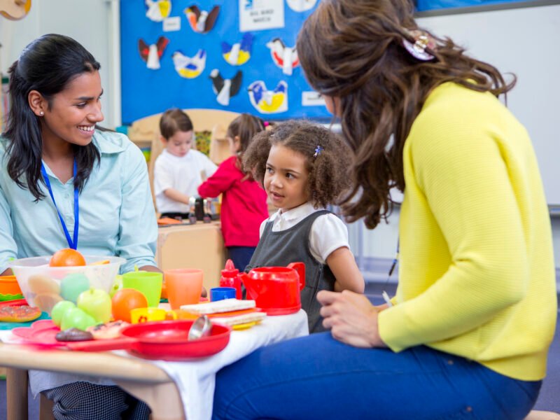 Roleplay Kitchen at Nursery Teachers playing with plastic kitchen toys with their nursery students in the classroom.